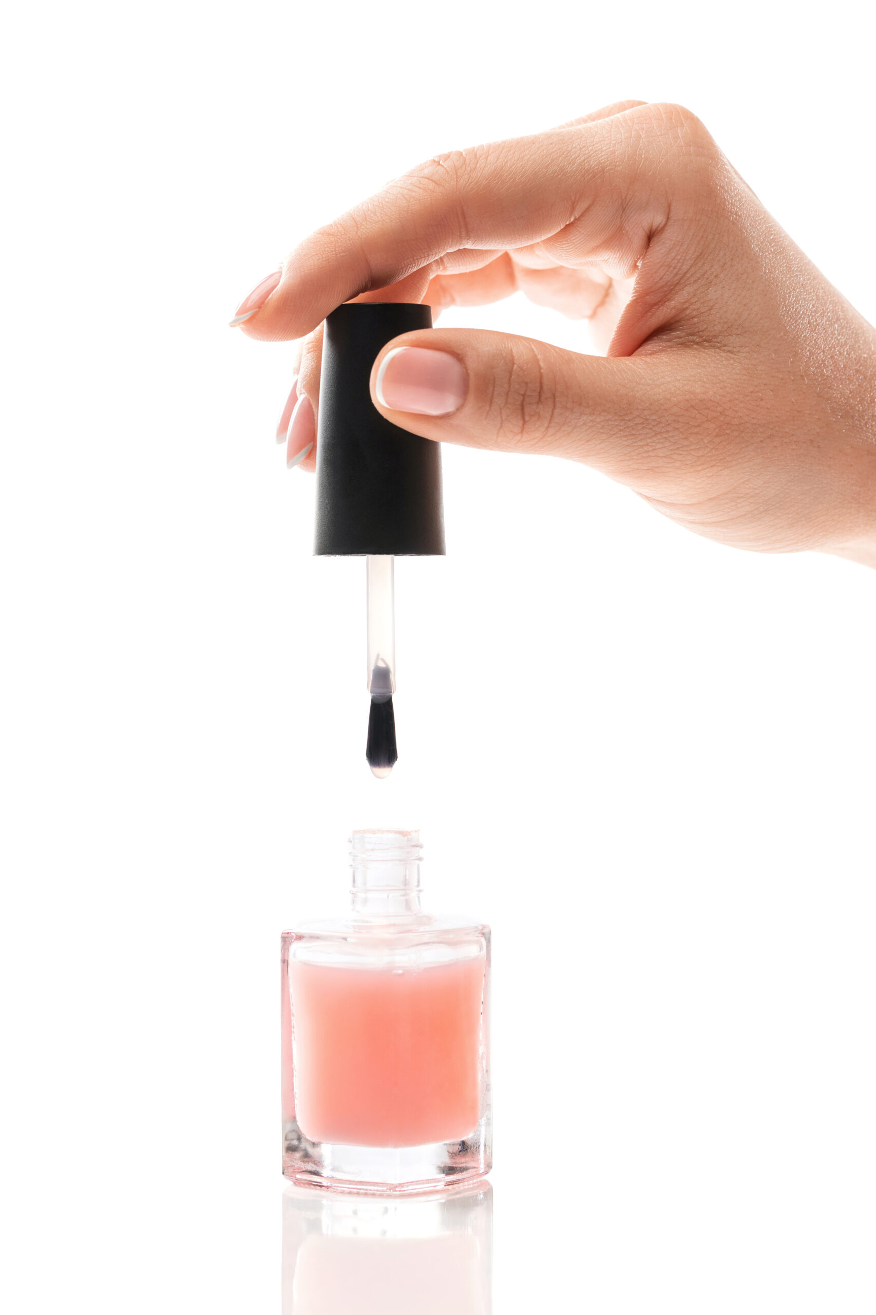 Closeup of female hand with beautiful french manicure holding bottle of pink nail polish against white background